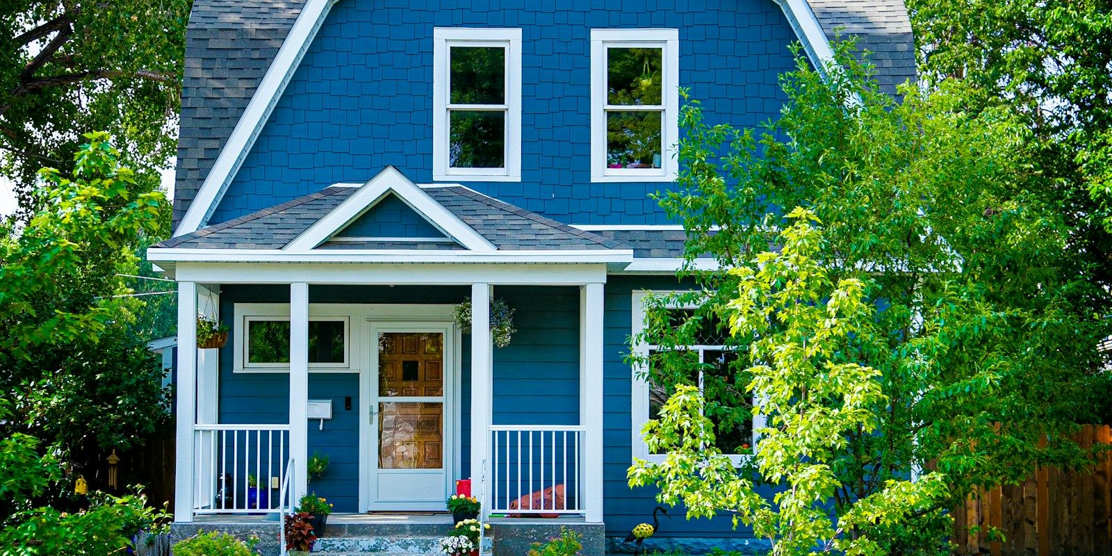 A blue and white colonial-style house among green trees