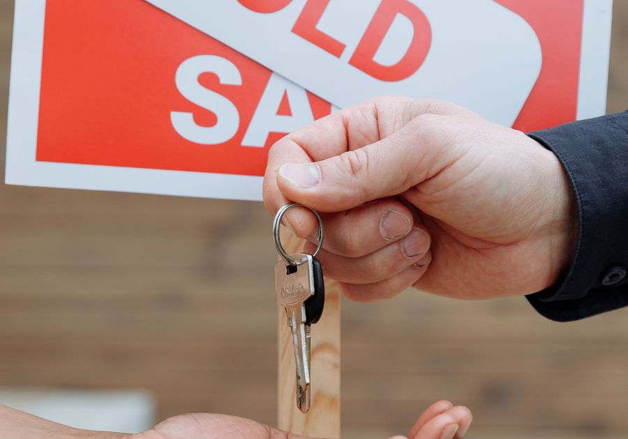 House keys being handed over in front of a Sold sign